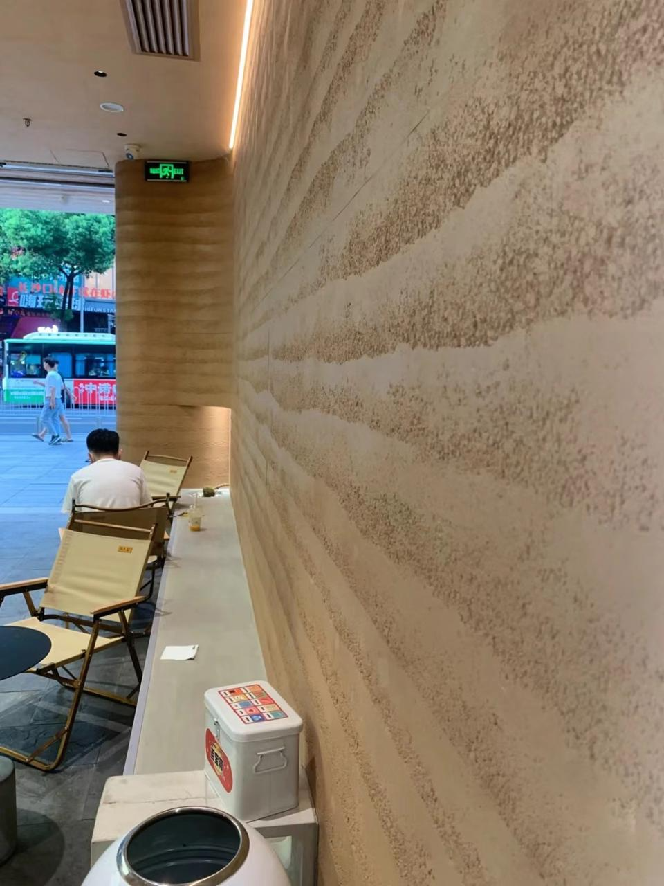 Rammed-earth textured wall lining a daylit café interior